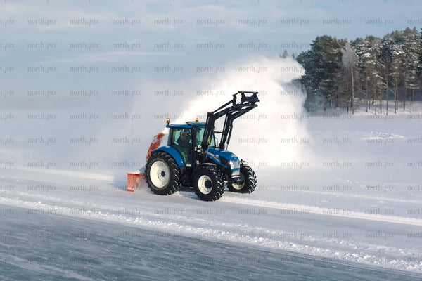 Blue tractor with snow plow clearing snow in open field under winter sky near forest