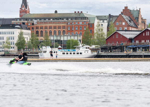 Jet ski passing passenger boat along Luleå waterfront, summer