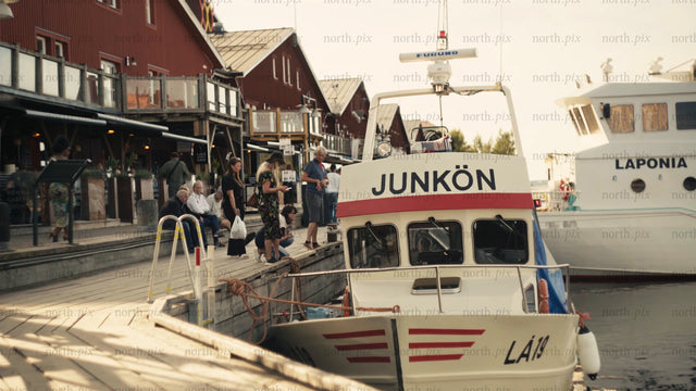 Luleå urban summer scene: People relaxing by the red houses on the pier at golden hour