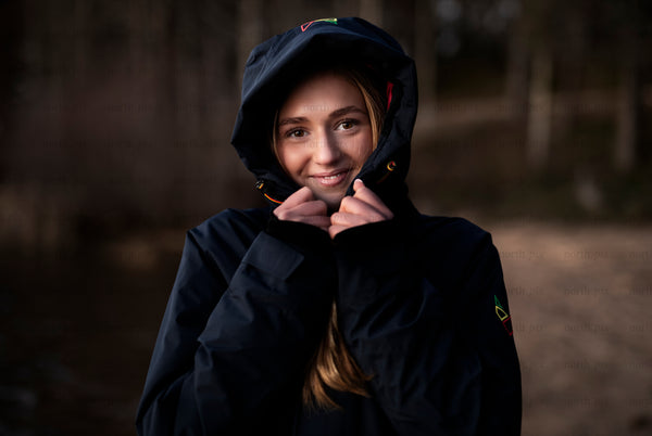 Young woman in hooded jacket by forest at dusk