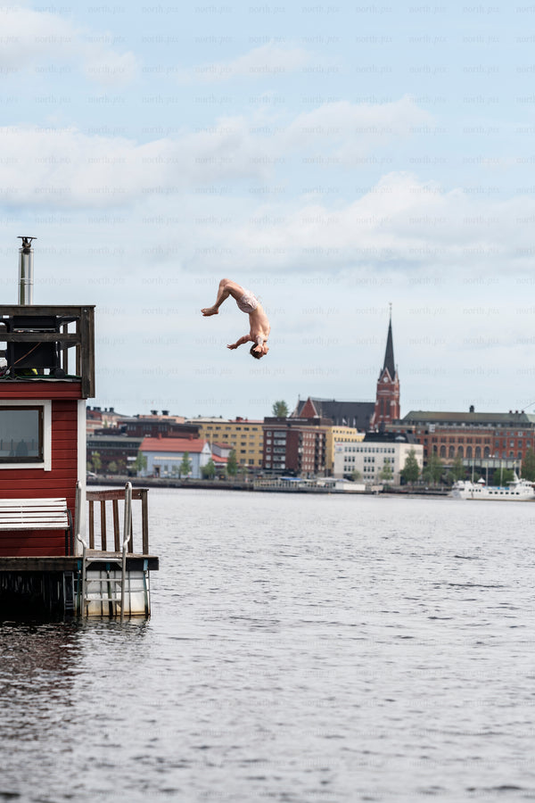 Man diving from dock over water with city skyline, daytime