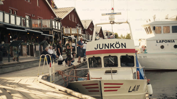 Luleå urban summer scene: People relaxing by the red houses on the pier at golden hour