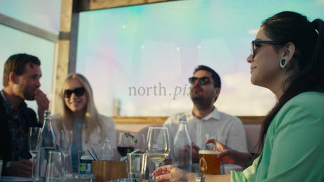 Friends Enjoying Drinks and Conversation at a Rooftop Restaurant in Lulea, Sweden During Sunset