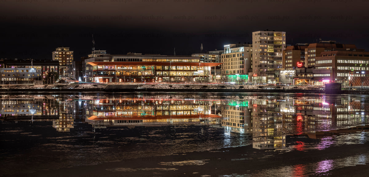 Byggnader vid floden reflekteras i isigt vatten på natten