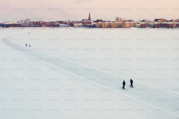 Snowy lake foreground with city center skyline of Luleå during winter calm soft sunset view