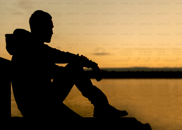 Silhouette of man sitting on dock at sunset