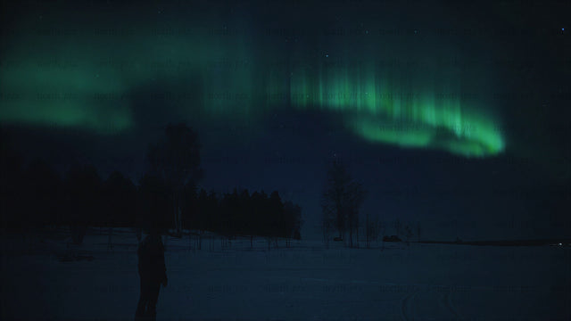 Person walking on a frozen lake under northern lights