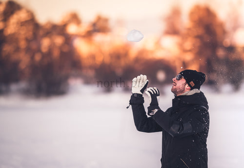 Man tossing snow in winter field at sunset