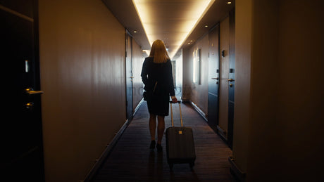 Businesswoman Walking Down Hotel Hallway with Suitcase Towards Bright Window