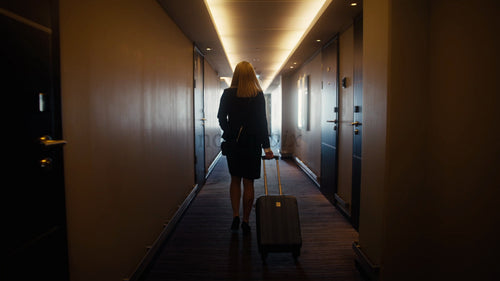 Affärskvinna går nerför hotellhallen med resväska mot ljust fönster