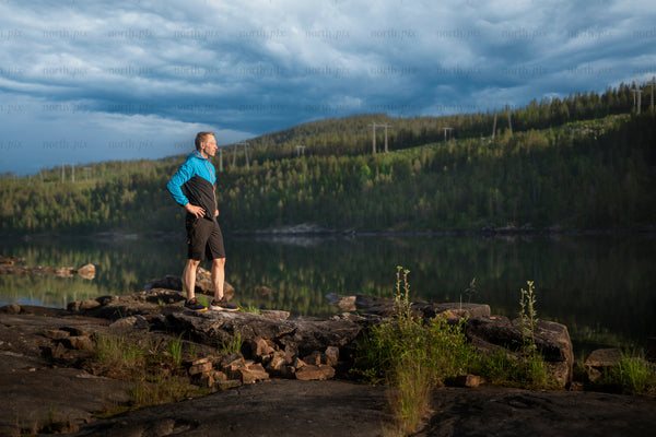 Man standing on rocky lakeshore at dusk, summer