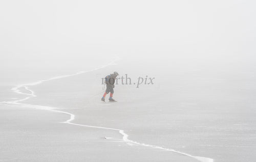 Skier crossing frozen lake in fog on winter day