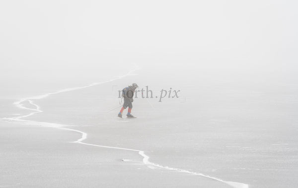 Skier crossing frozen lake in fog on winter day