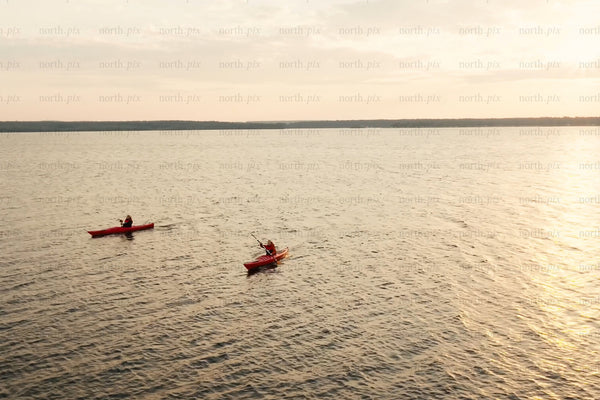 Two red kayaks paddling on sunset lake, water scene overlooked by distant shore