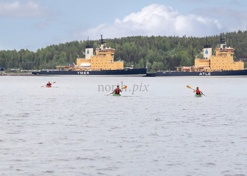 Kayakers paddling near docked icebreakers on overcast day