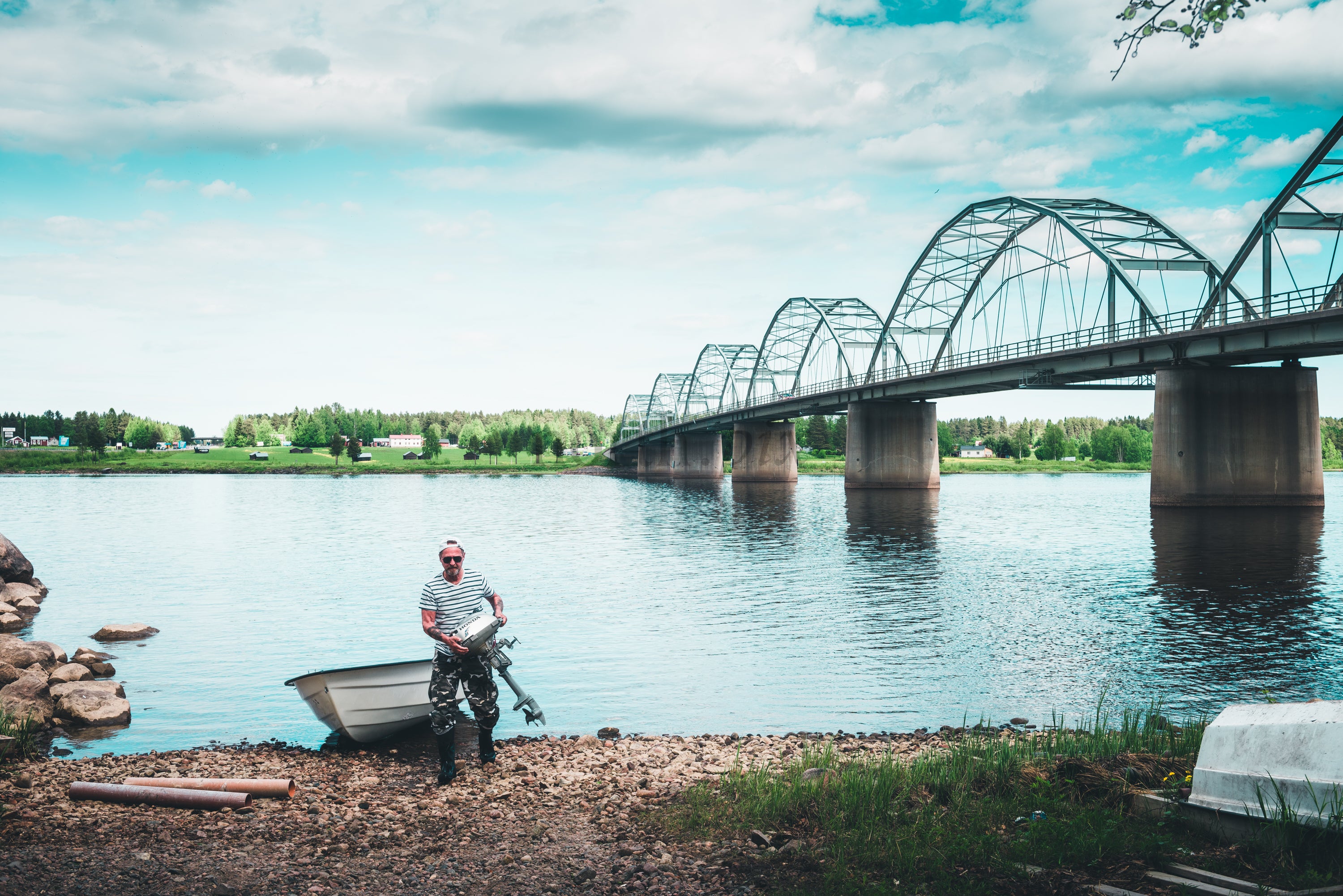 Man with outboard motor on riverbank under arched bridge, summer