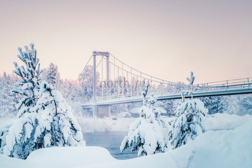 Snötäckt hängbro över en vinterflod