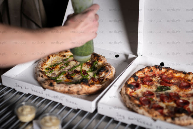 Hand squeezing pesto over pizza in takeout box