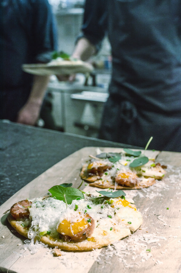 Chefs plating flatbread with cheese in a kitchen