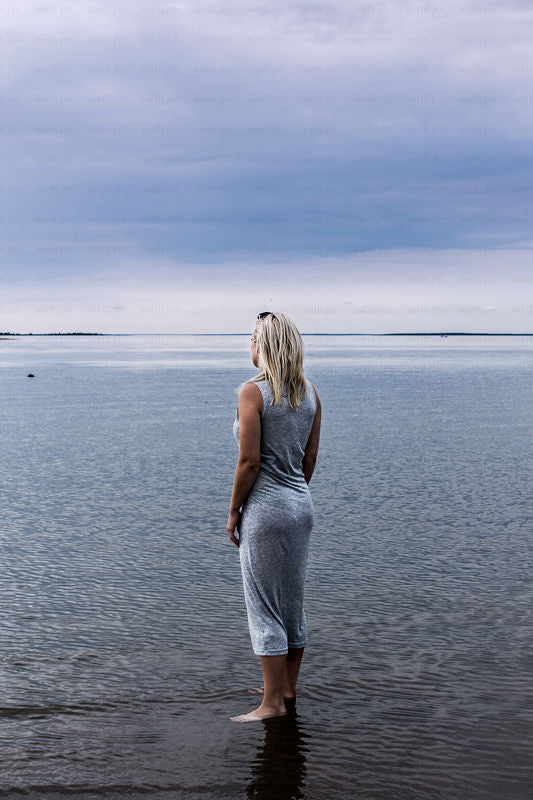 Woman standing on shoreline looking toward horizon, daytime