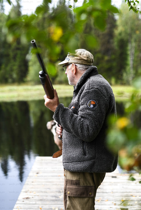 Man with shotgun on lakeside dock in autumn morning