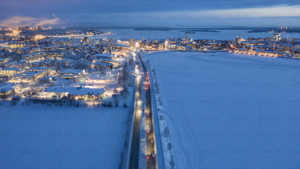 Aerial dusk timelapse of snowy Luleå, in winter: Cars on roads, frozen bay