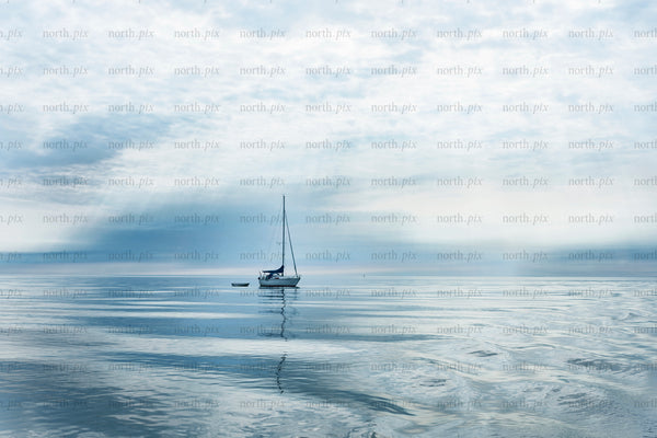 Sailboat anchored on calm sea under cloudy sky