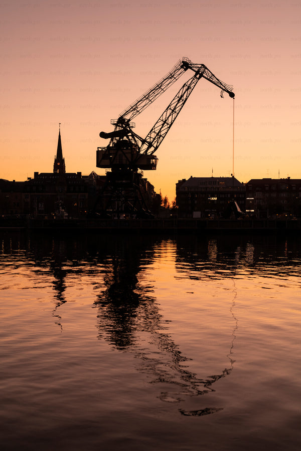 Silhouette of harbor crane and city at sunset
