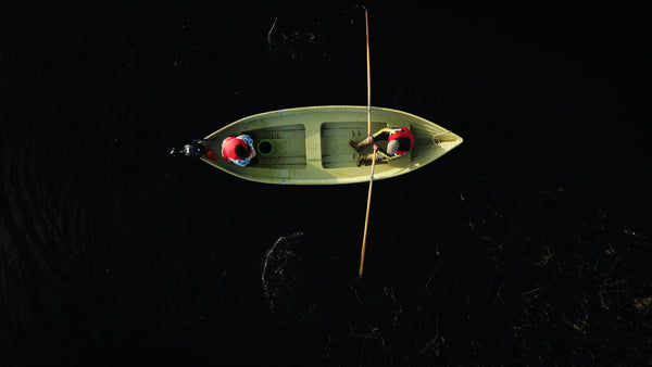 Summer crayfish fishing: Two people rowing a small boat on a dark lake in Luleå