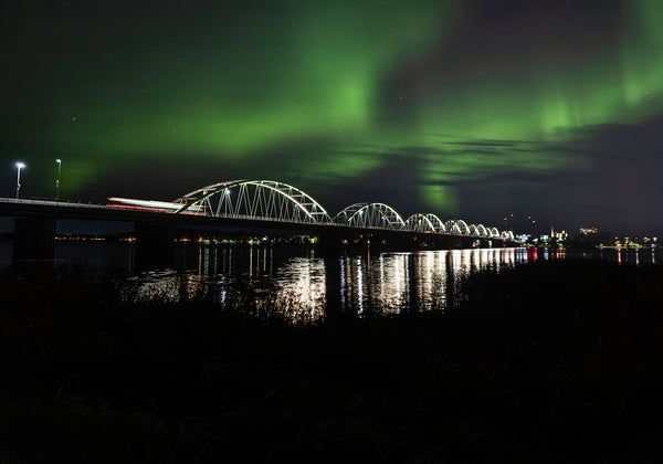 Arch bridge under Northern Lights over river at night
