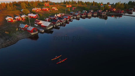 Kayakers Paddle Past Red Cabins in the Luleå Archipelago at Sunset