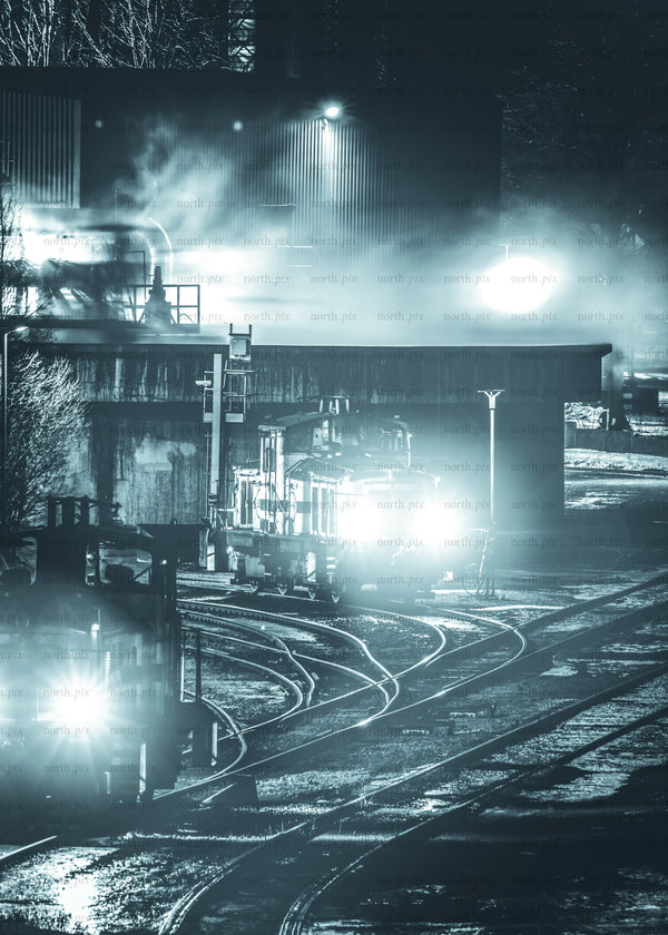 Locomotives in rail yard at night with headlights