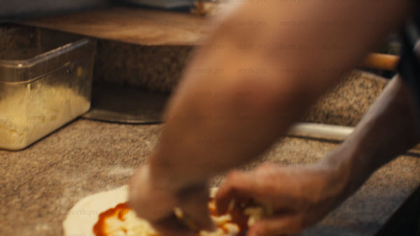 Chef prepares pizza with tomato sauce, mozzarella, and bell peppers in a professional kitchen
