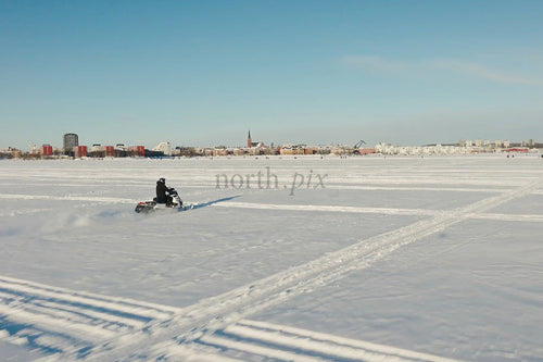 Snöskoteråkare över öppet snöfält mot Luleå centrum på en klar vinterdag
