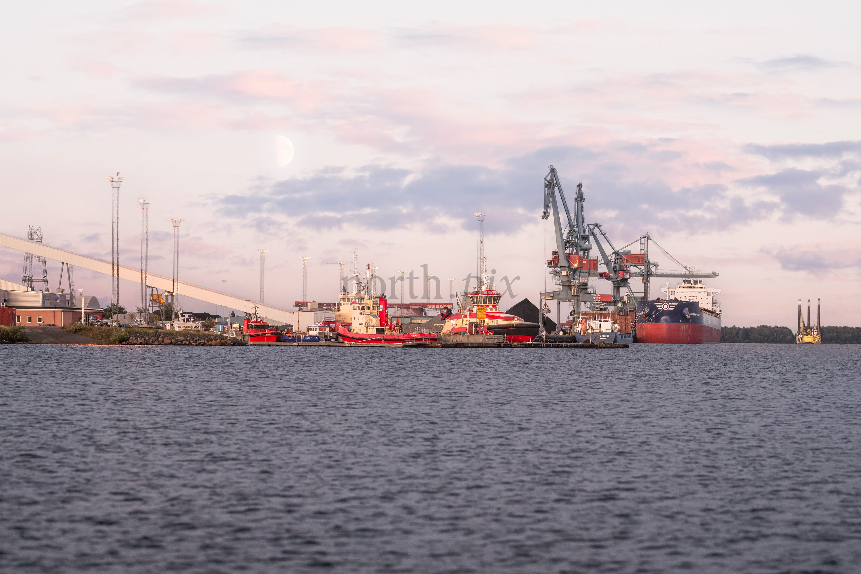 Cargo ship and cranes at industrial harbor at dusk