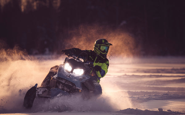 Snowmobile rider on snowy field at sunset