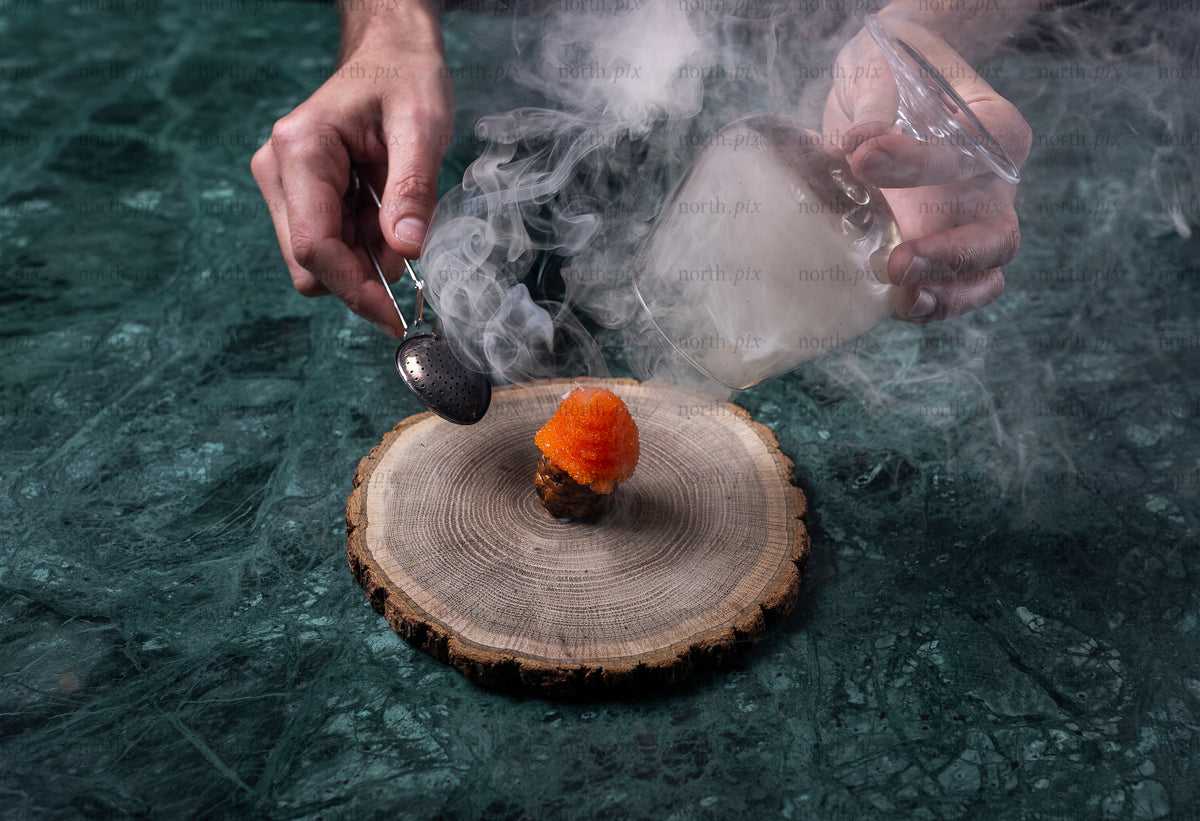 Hands smoking an appetizer on a wood slice