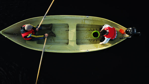 Two men rowing a boat on a dark, still lake in Luleå, summer day