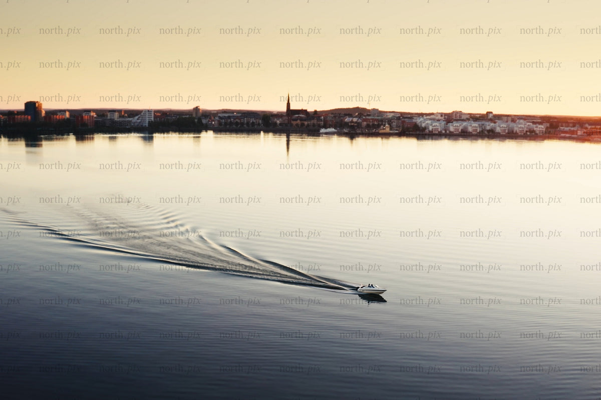 Boat glides across calm water toward Luleå city center at sunset