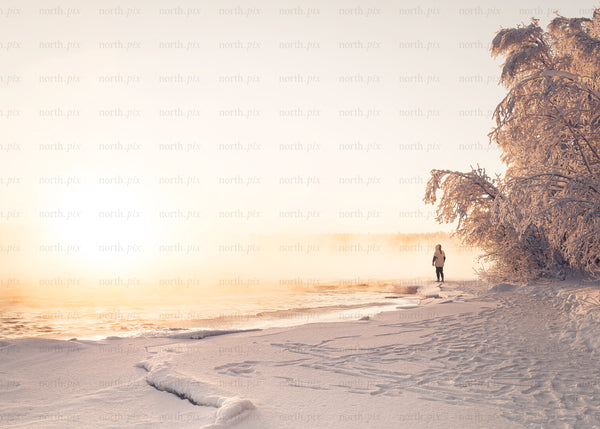 Person walking on snowy shore at sunrise
