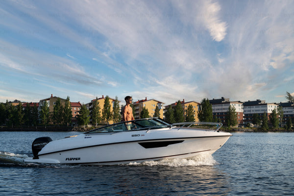 Man steering motorboat by riverside apartment buildings at sunset