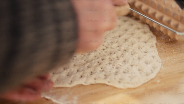 Hands imprinting dough with patterned rolling pin on wooden board