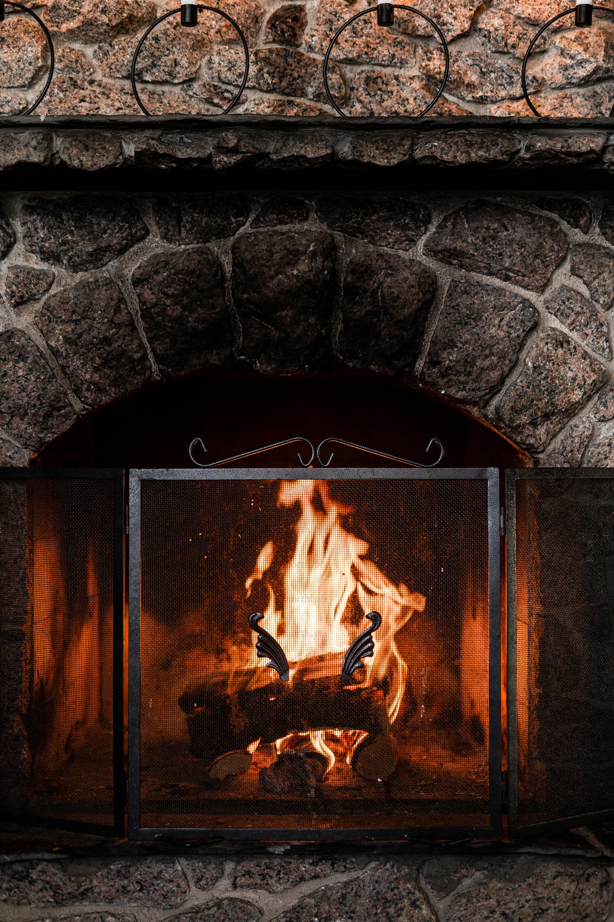 Stone fireplace with burning logs and metal screen