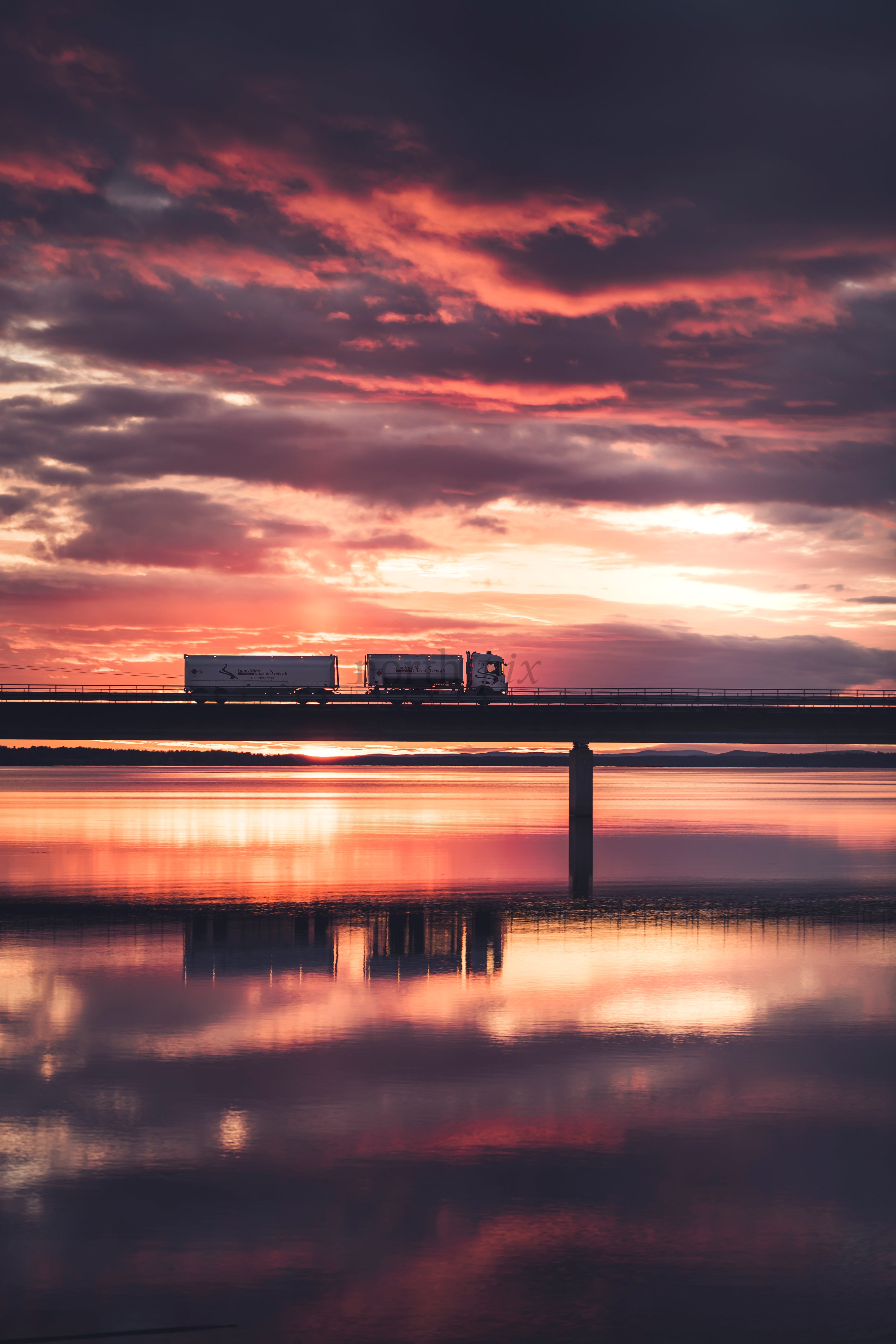 Truck crossing bridge at sunset with water reflection