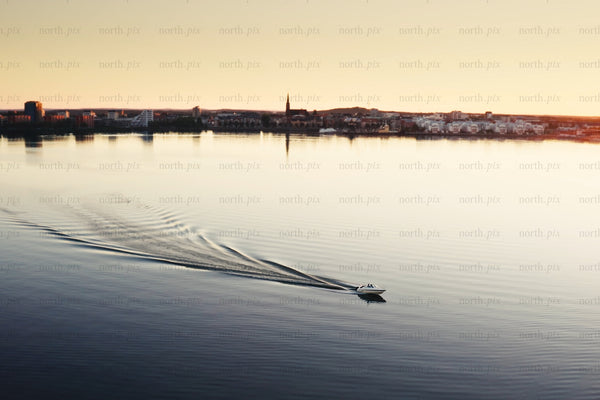 Boat glides across calm water toward Luleå city center at sunset