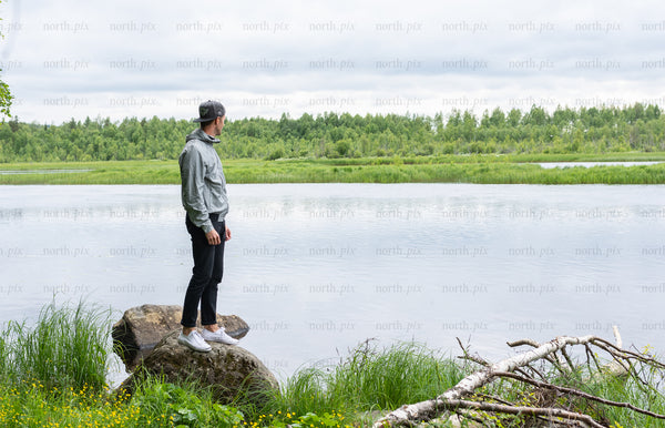 Man standing on rock by river under cloudy sky