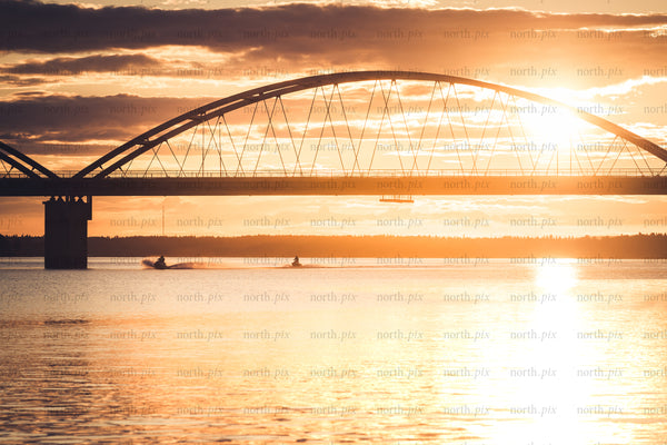 Arch bridge at sunset over calm water with jet skis