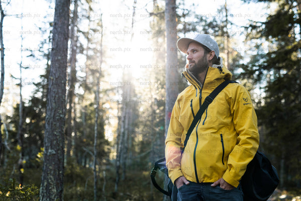 Man in yellow jacket standing in forest late afternoon
