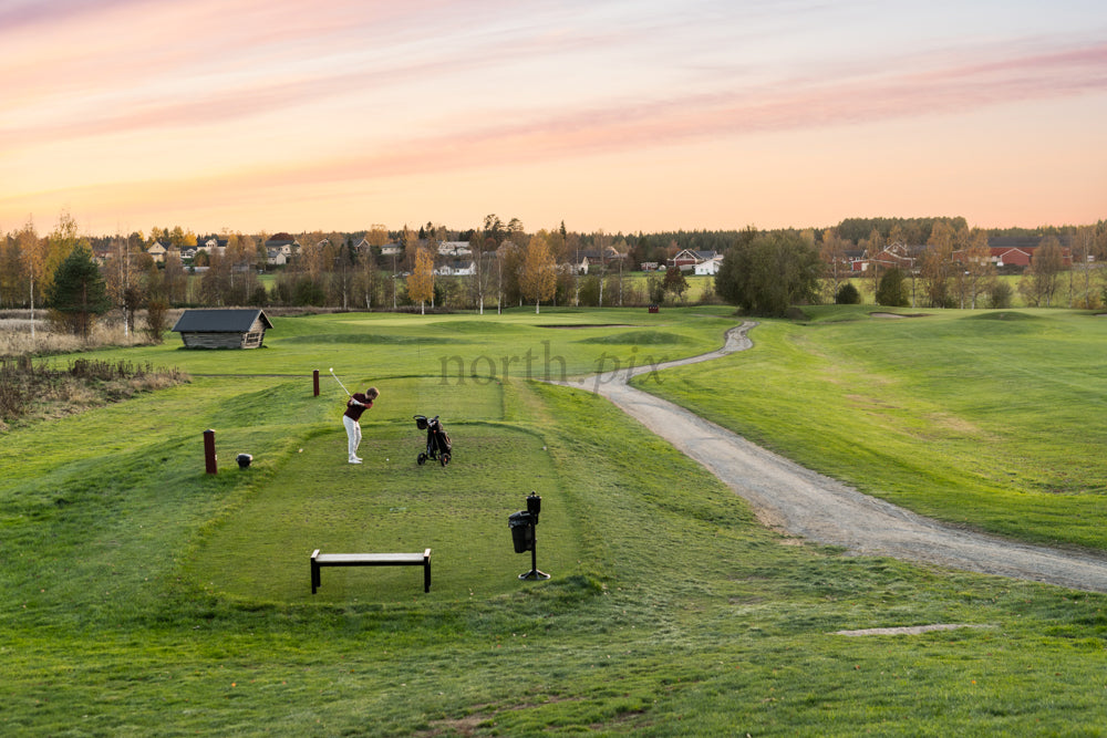 Golfer teeing off on golf course at sunset