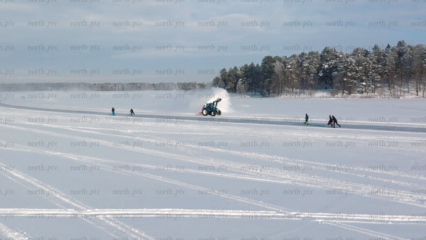 Tractor clearing snow on frozen lake in Luleå, with people skating and kick sledding